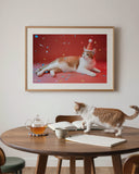 "The Gallery Wall" by YOUNI.ONE. An elegant dining room styling mockup showcasing a custom bespoke orange and white cat portrait in a light wood frame. The museum-grade statement piece features our signature vibrant red Studio Edit background, effortlessly complementing the modern wood interior aesthetic.